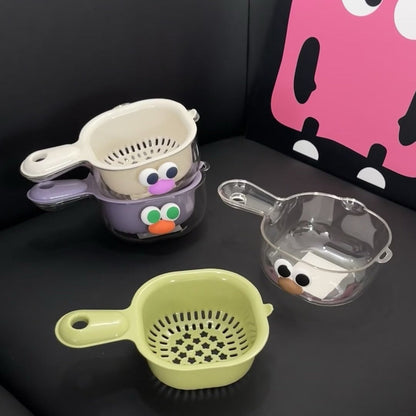 Three colorful kitchen strainers with cartoon face designs on a dark surface.