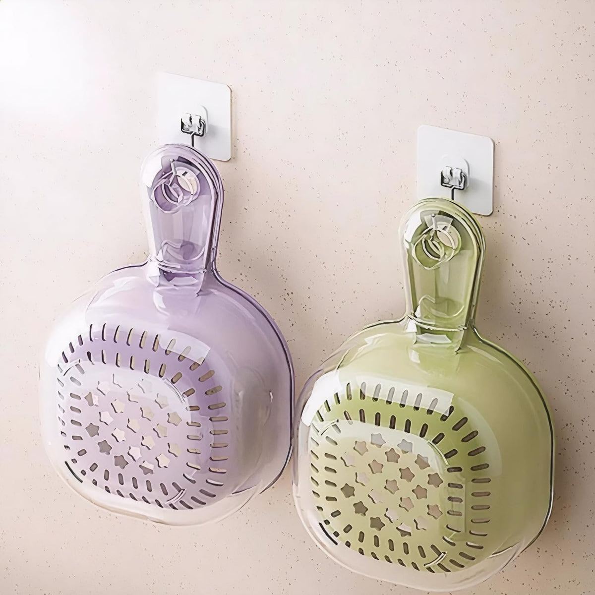 Two wall-mounted kitchen strainers, one purple and one green, on a light-colored wall.